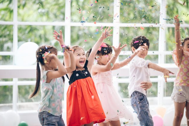 Group of children throw their arms in the air under confetti