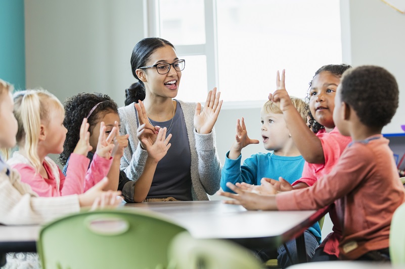 Children and educator sitting at table playing a clapping game