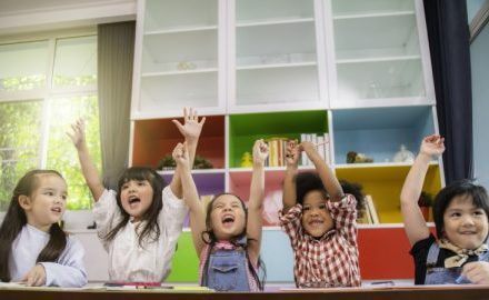Preschool aged children in an education and care setting, celebrating with arms raised