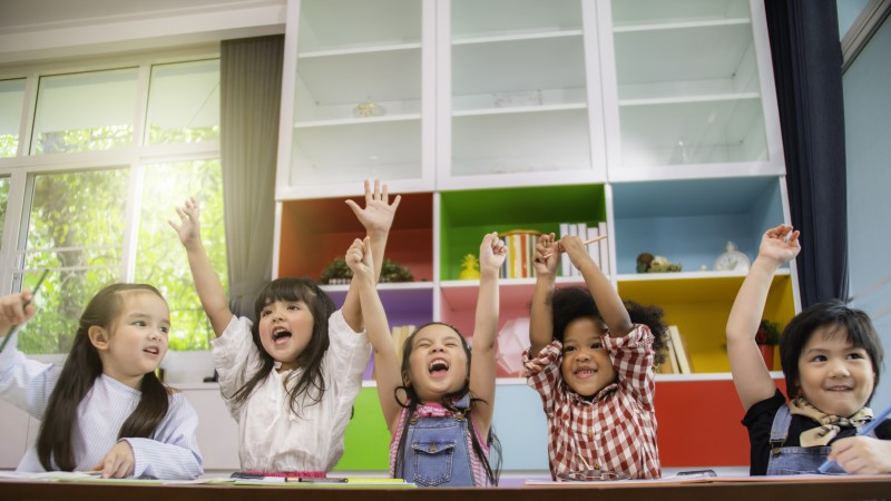 Preschool aged children in an education and care setting, celebrating with arms raised