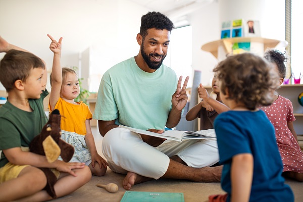 Educator sitting on the ground with children, holding up two fingers