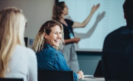 Educator at a conference, looking over her shoulder, smiling and enjoying the presentation