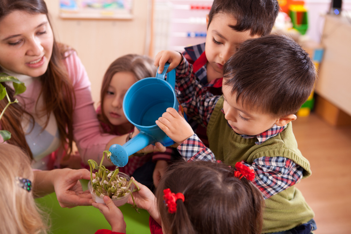 Educator supporting children to water a plant