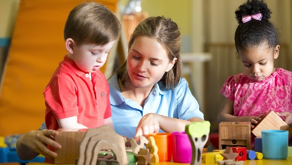 Educator sitting with children at a table using wooden stacking toys