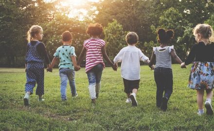 Children in a row holding hands and running through a park