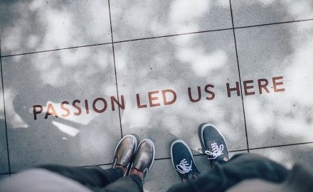 View of two pairs of feet in front of sign painted on the ground reading: Passion led us here