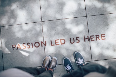View of two pairs of feet in front of sign painted on the ground reading: Passion led us here