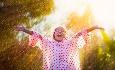 Happy child wearing spotty rain coat stretching arms to the sky
