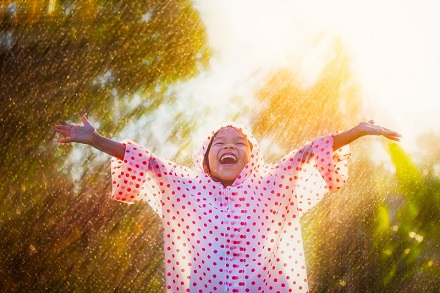 Happy child wearing spotty rain coat stretching arms to the sky
