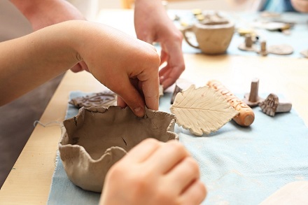 Child's hands making a small clay pot