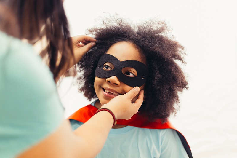 Educator adjusting superhero mask on child