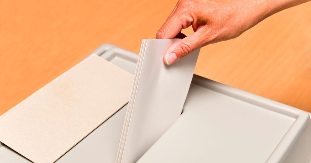 Hand putting envelope into ballot box