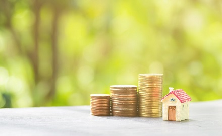 Three piles of coins next to small house figurine