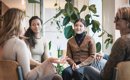 Group of women sitting in a circle talking, plants in the background
