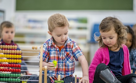 Two children playing together on the group next to an abacus