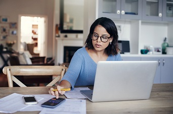 Educator sitting at desk infront of laptop using a calculator