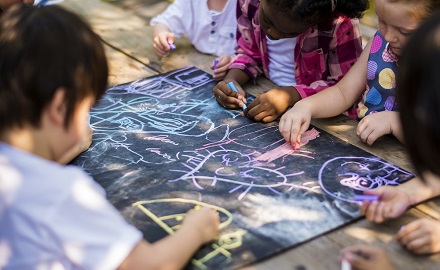 Group of children drawing on a chalk board outdoors on the ground