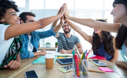 Five adults sitting around a table high fiving