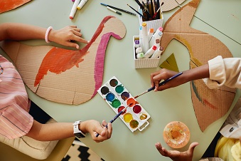 Children using paint supplies to paint cardbopard animal cutouts, viewed from above.